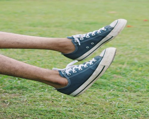 A relaxed individual wearing comfortable canvas sneakers walking casually on a city sidewalk alongside a public park border