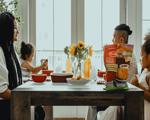 A group of adult family members sitting around a brightly lit dining table laughing and talking together in harmony