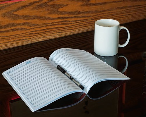 A classic ceramic coffee mug resting on an open journal notebook next to an office workspace during midday break