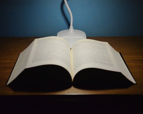 A soft warm bedside table lamp illuminating pages of an open physical hardcover book ready for reading